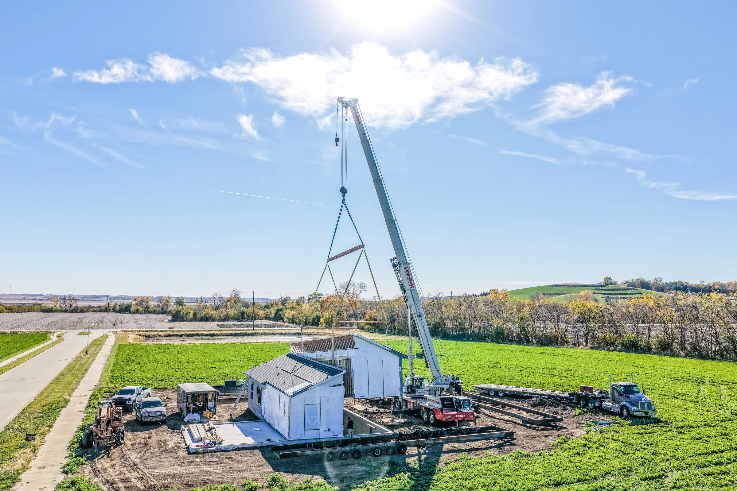 A modular home being lifted into place by a large crane in a rural field
