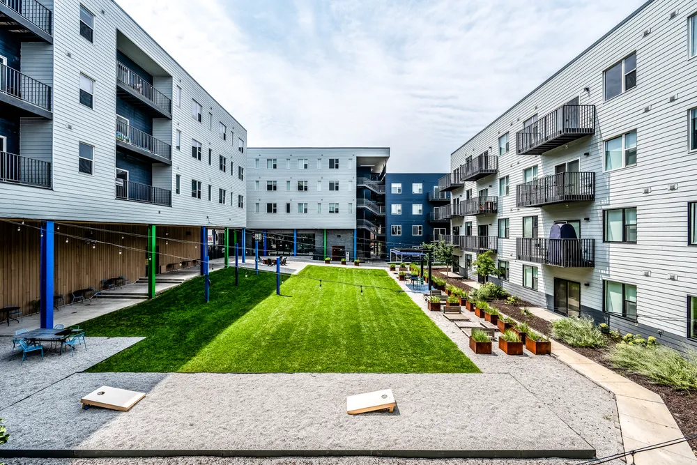 Apartment courtyard with a lawn, cornhole boards, and string lights