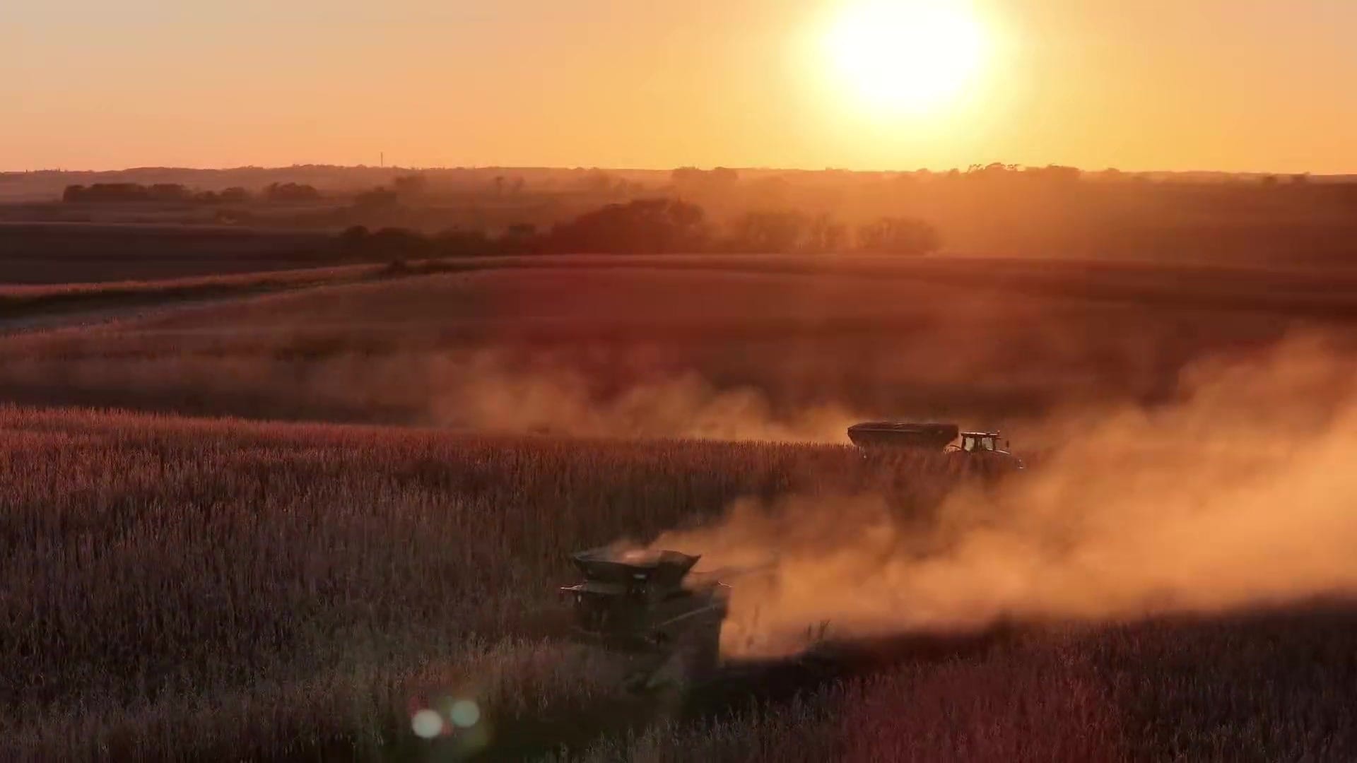 Aerial view of a combine harvester working a field at golden hour, dust trailing behind it